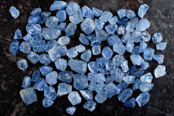 Collection of lovely blue rough and uncut sapphire gemstones on black stone slate.