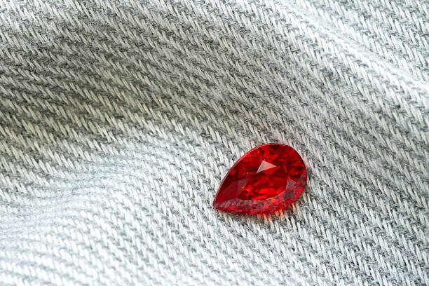 Red ruby gemstone with pear cut shape placed on denim fabric background, symbolizing passion, luxury, elegance, fashion accessories, and modern jewelry design inspiration.