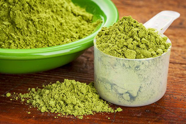 measuring scoop of moringa leaf powder with a bowl on wooden surface