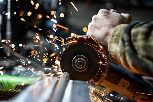 Metalworker operating an angle grinder actively cutting on a metal surface, emitting dynamic sparks. Depicts craftsmanship, industrial labor, and the creative sparks of manufacturing processes under precise control.